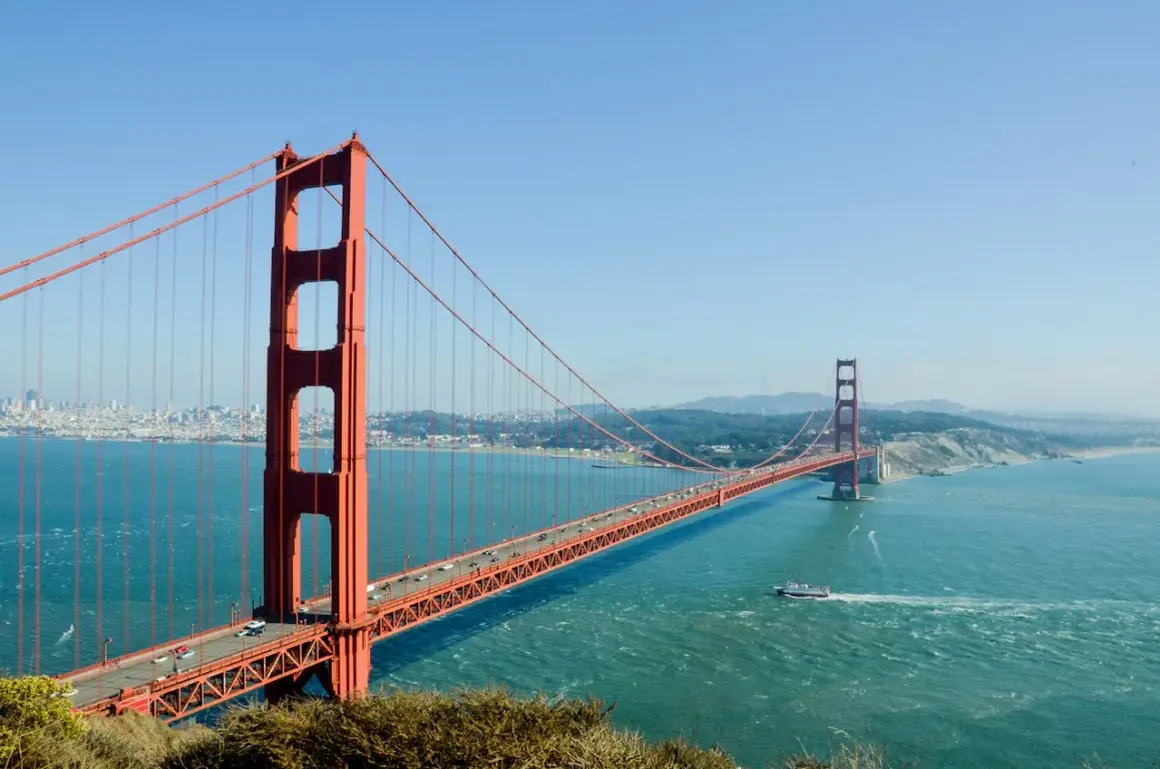 Most znany na świecie, Golden Gate Bridge w San Francisco, z ruchem samochodowym i łodzią na wodzie.