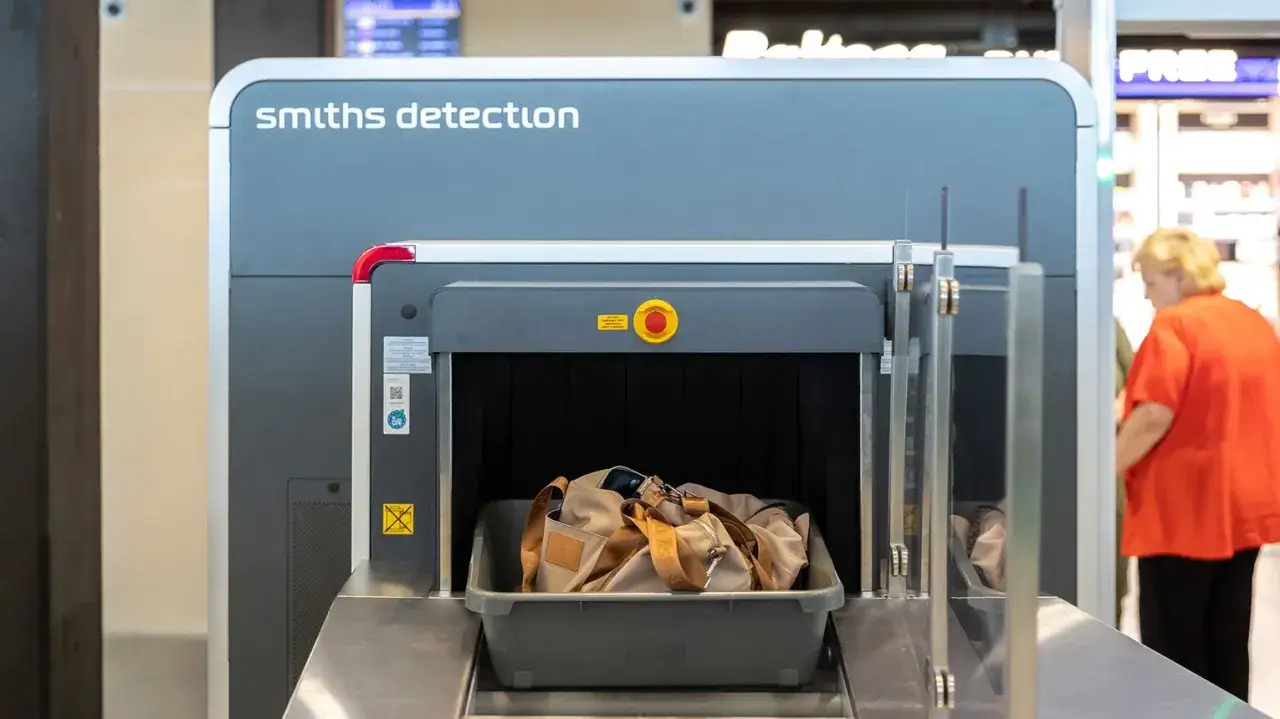 Skaner bagażu Smiths Detection z torbą w tacce i kobietą w tle.